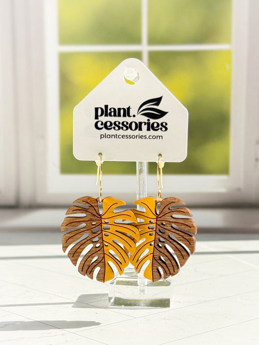 Handmade wooden monstera leaf earrings, yellow on one side and stained wood on the other, hanging on a Plant.cessories display card.