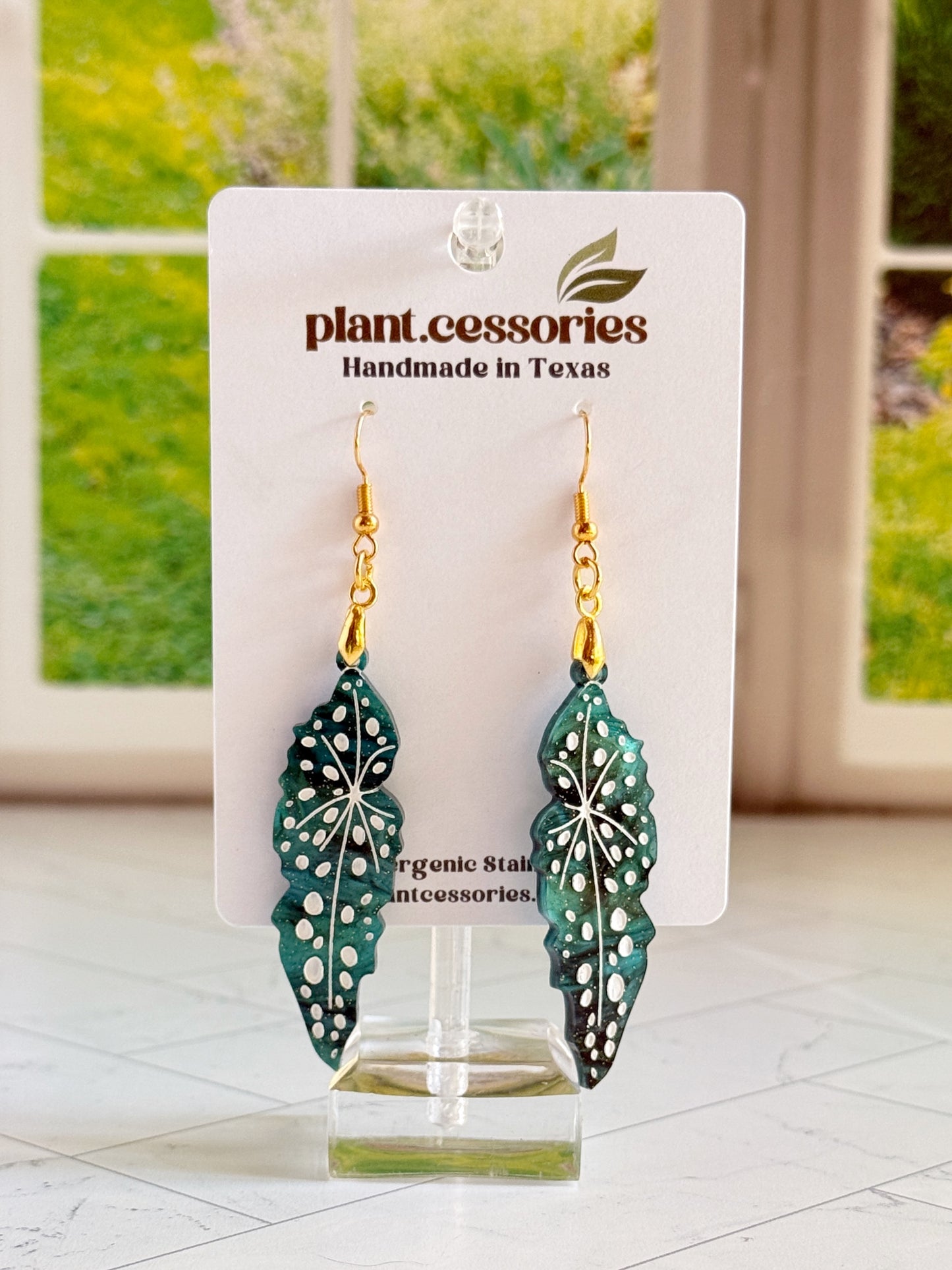Close-up of shimmery green Begonia maculata earrings with white hand-painted details.