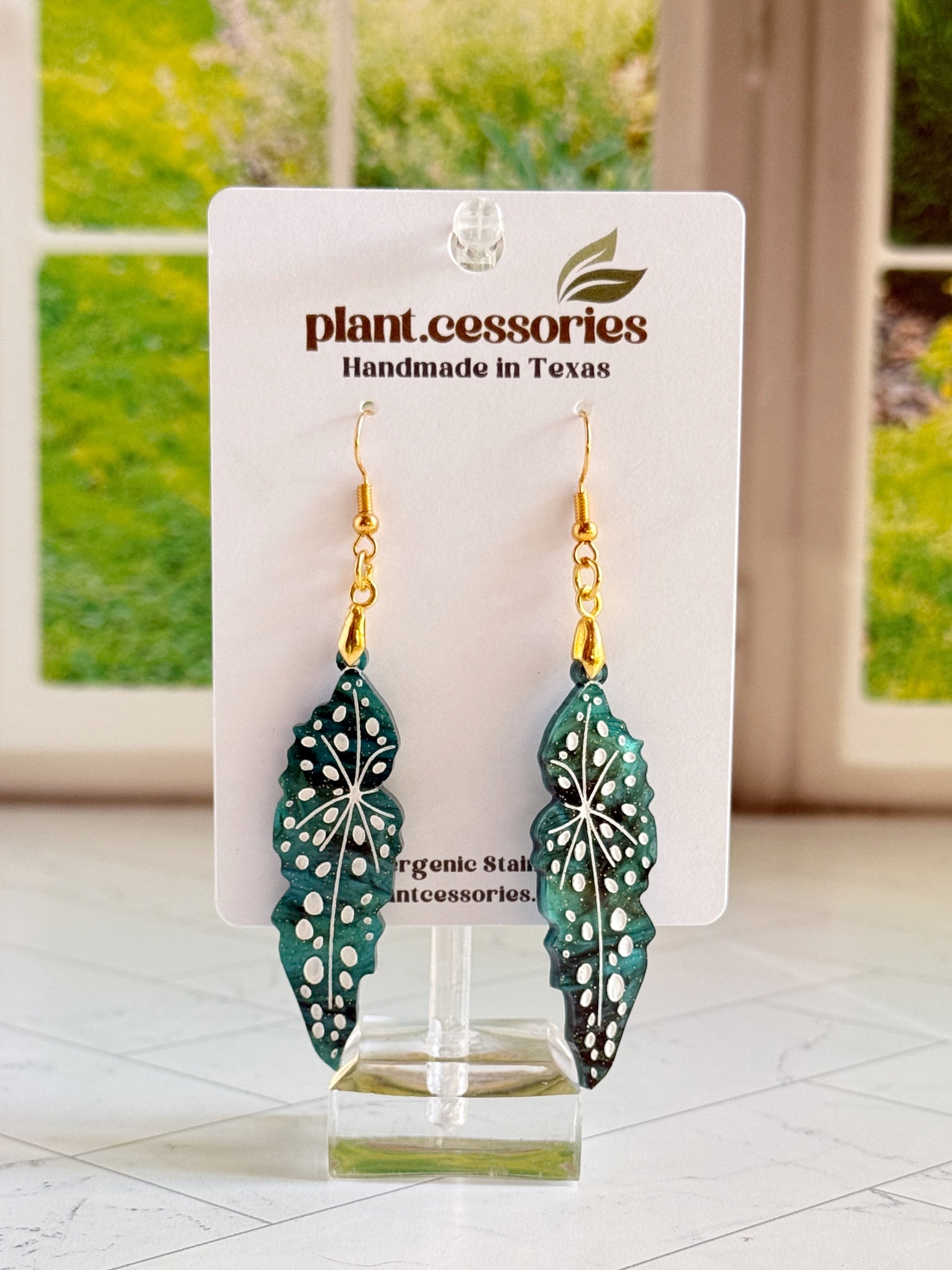 Close-up of shimmery green Begonia maculata earrings with white hand-painted details.