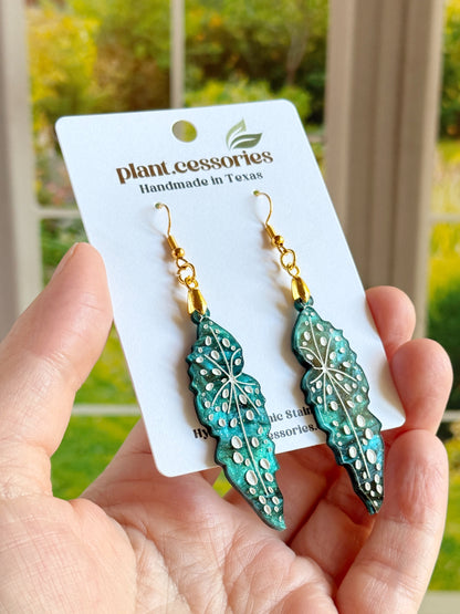 Close-up of shimmery green Begonia maculata earrings with white hand-painted details.