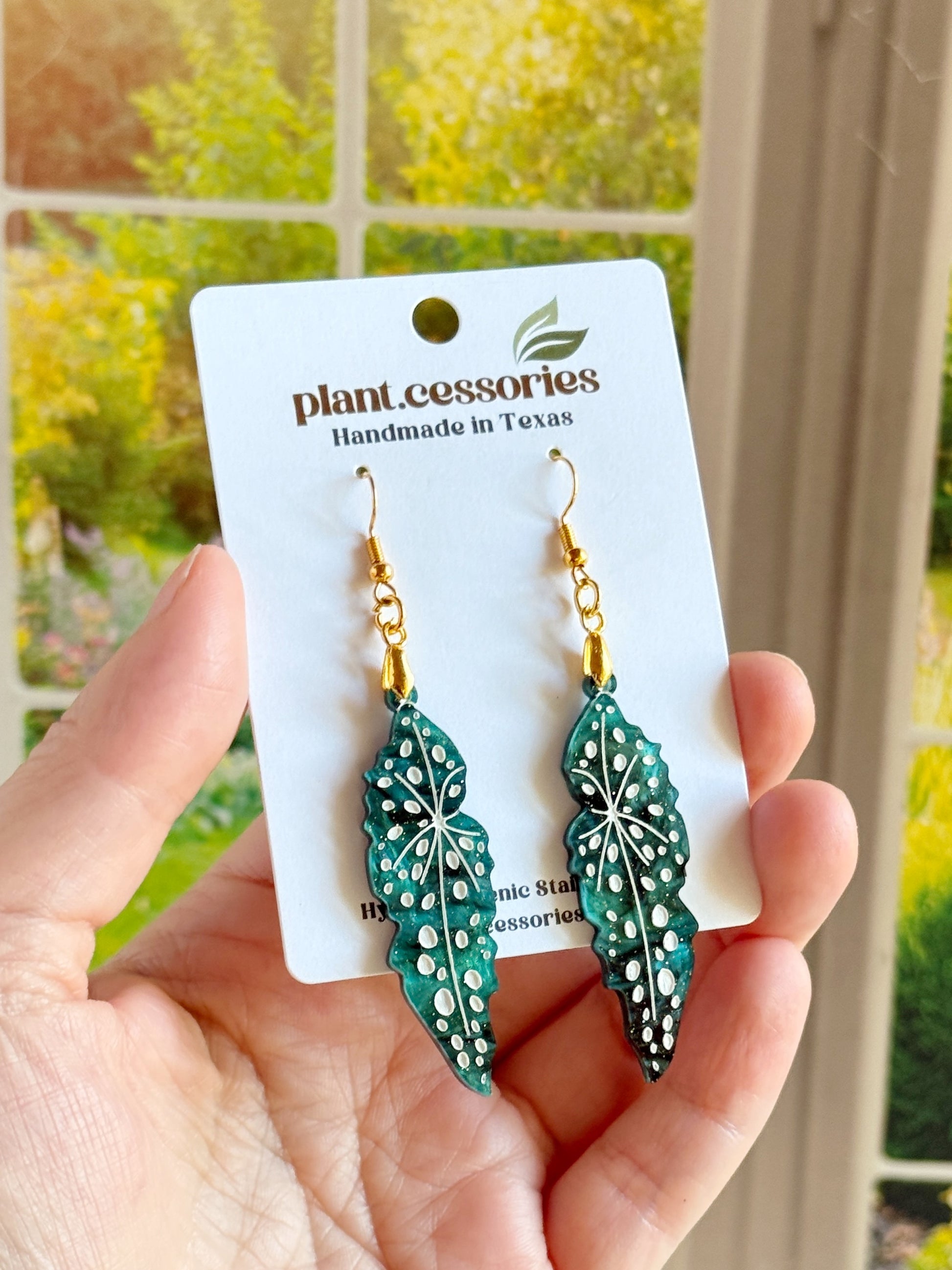 Close-up of shimmery green Begonia maculata earrings with white hand-painted details.