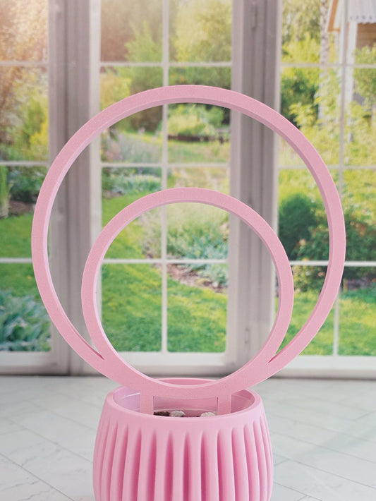 Pink double hoop plant trellis placed in a ribbed pink planter near a bright window