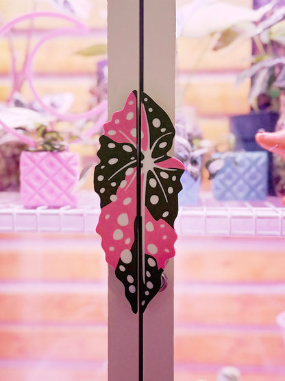 Variegated Begonia maculata cabinet handle covers with pink and green spotted leaf design on a white milsbo tall cabinet.